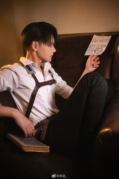 a person sitting on a couch with a book in his lap and wearing suspenders