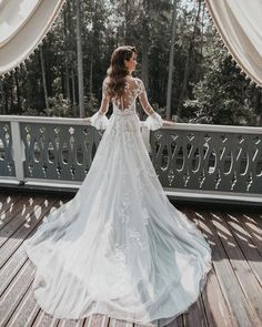 a woman in a white wedding dress standing on a deck looking out at the woods