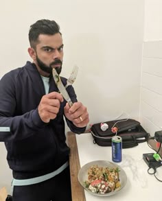 a man holding a fork and knife over a plate of food on a counter top