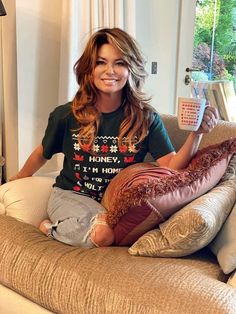 a woman sitting on top of a couch holding a coffee cup and smiling at the camera