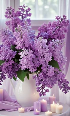 a vase filled with purple flowers sitting on top of a table next to lit candles