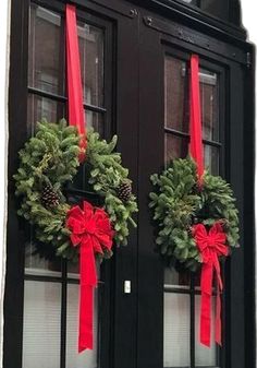 two wreaths on the front door of a house with red bows and pine cones