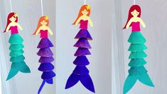 three different colored paper mermaids hanging from strings