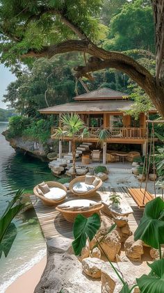 a wooden dock with chairs and tables on it near the water in front of a house