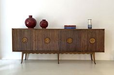 a wooden cabinet with two vases on top of it next to a white wall