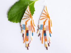 a pair of beaded earrings on top of a green leaf next to a white background