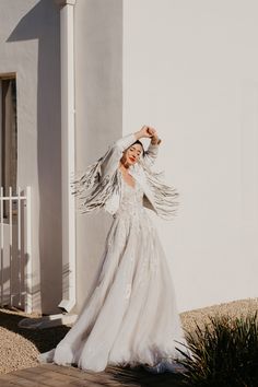 a woman standing in front of a building wearing a long white dress with feathers on it