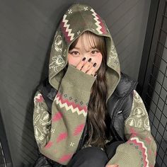 a young woman sitting on the floor wearing a sweater and mittens, covering her face with both hands