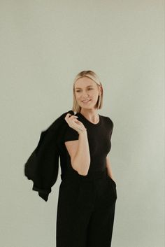 a woman standing in front of a white wall wearing black pants and a black top