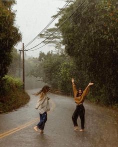 two people jumping in the rain on a road with trees and telephone wires above them