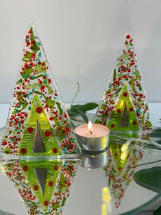 two christmas trees sitting on top of a glass table next to a candle and some leaves