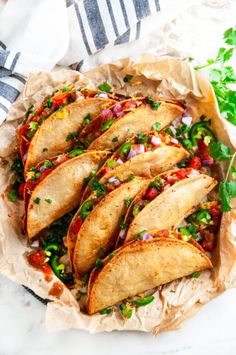 some tacos are sitting in a basket on top of paper and garnished with cilantro