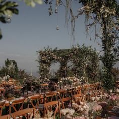 an outdoor wedding set up with wooden chairs and tables covered in flowers, surrounded by greenery