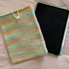 a cell phone is laying next to a knitted pouch on a bed with pink sheets