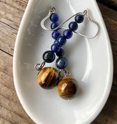 Charming blue Lapis Lazuli and gold Tiger Eye earrings are stunning. These cool 2.25 inch earrings are elegant enough that they would Step up your style game with these stunning earrings, featuring a gorgeous combination of Tiger Eye and Lapis Lazuli. The natural earthy tones of the gemstones make these earrings a versatile accessory that can be dressed up or down, depending on the occasion. With their sophisticated design, these earrings are perfect for a formal setting, but also versatile enou Blue Spiritual Earrings For Gifts, Spiritual Blue Jewelry For Birthday, Spiritual Blue Jewelry For Birthdays, Spiritual Blue Jewelry For Mother's Day, Blue Jewelry With Matching Earrings For Mother's Day, Blue Dangle Jewelry For Mother's Day, Blue Dangle Jewelry For Birthday, Blue Dangle Earrings For Mother's Day, Earrings Handmade Boho