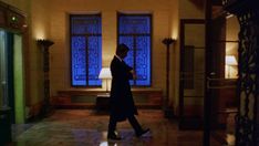 a man in a suit walks through an empty room with large windows and floor tiles