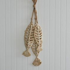 two fish hanging from a rope on a white wall next to a wooden hook with string