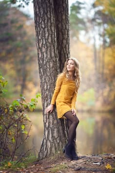 a beautiful young woman leaning against a tree in front of a lake wearing black tights