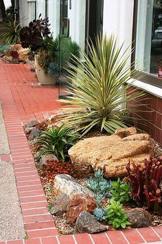 a red brick sidewalk with plants and rocks on the side walk next to a building