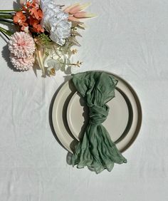 a white plate topped with a green napkin next to flowers