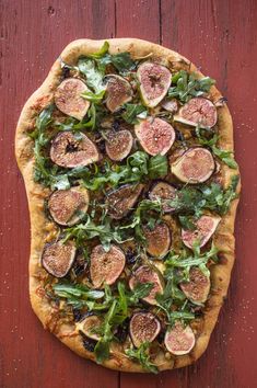 a pizza topped with figs and greens on top of a wooden table next to a red wall