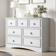 a white dresser with flowers and pictures on the wall