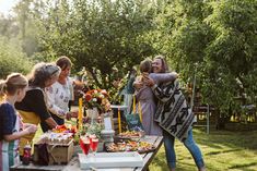 a group of people standing around a table with food and drinks on top of it