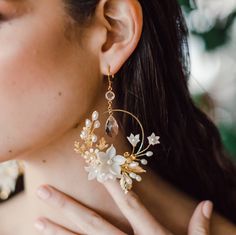 "Our Blyth floral and leaf bridal earrings are so romantic and perfect for the modern bride who wants showstopping wedding jewelry. Available in silver and gold, these gorgeous large hoop earrings feature handscuplted clay flowers, leaves, crystals and pearls.  Wear these earrings with a romantic lace wedding dress, or make them modern with a simple silk gown.  Beautifully accented with plated oak and rose leaves and clustered with a bouquet of hand sculpted clay flowers in various sizes, hand p Gold Flower Hoop Earrings For Wedding, Gold Floral Hoop Earrings For Wedding, Delicate Flower Hoop Earrings For Weddings, Handmade Flower Earrings For Wedding, Flower Hoop Earrings For Wedding, Vine Earrings, White Flower Earrings, Romantic Wedding Dress Lace, Earrings For Bride