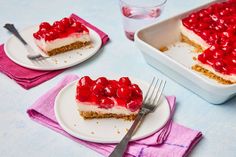 two plates with slices of cheesecake covered in cherries and crumbs next to a glass of water