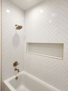 a bathroom with white and gold herringbone tile on the walls, shower head, and bathtub