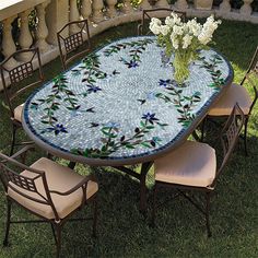 a mosaic table and chairs with flowers in vase on the top, set up outside