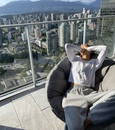 a woman laying on top of a chair in front of a cityscape with tall buildings