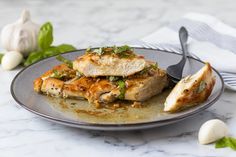 a plate topped with chicken covered in sauce and garnished with green herbs next to garlic