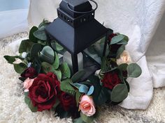 a black lantern with flowers around it on a rug