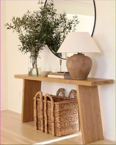 a wooden table topped with baskets and a lamp next to a vase filled with plants