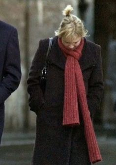 a woman in a red scarf walking down the street with a man wearing a suit and tie