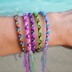 three bracelets are on the arm of a person at the beach with water in the background