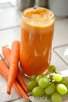 carrots and grapes sit next to a glass of juice