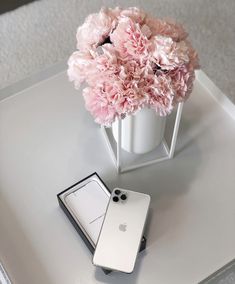 an iphone is sitting on a table next to a vase with pink flowers in it