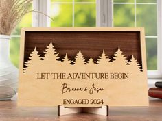 a wooden sign that says let the adventure begin with pine trees and lettering on it