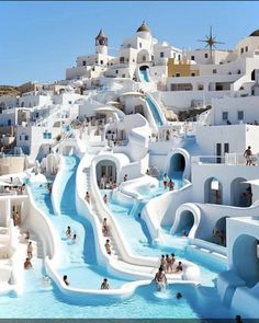 many people are swimming in the pool with slides and buildings on the hill behind them