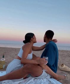 a man and woman sitting on top of a towel at the beach talking to each other