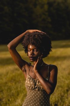 a woman standing in a field holding her hair up to her head and looking at the camera