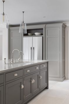 a large kitchen with gray cabinets and marble counter tops, two pendant lights over the sink