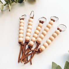 four wooden beaded keychains are shown on a white surface with greenery