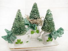 three white mugs with green plants in them on a tray, one has a bow