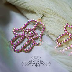 a pair of pink and green beaded earrings sitting on top of a white fur