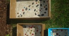 two boxes are sitting on the grass and one is filled with different colored glass beads