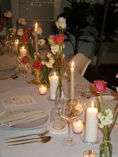 the table is set with candles and flowers in vases, plates and silverware