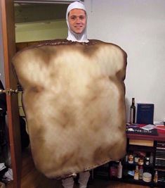 a man dressed in nun costume holding up a large piece of brown paper that looks like a giant slice of bread